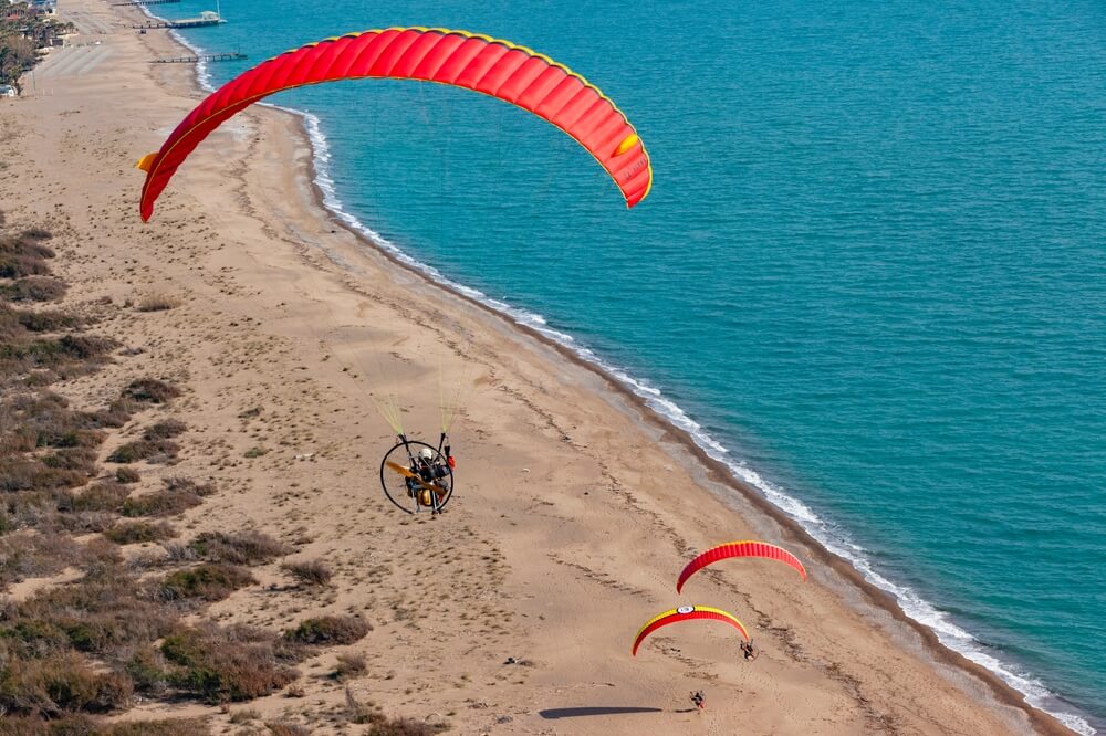 Paramotoroví piloti letiaci nad plážou v Beleku,